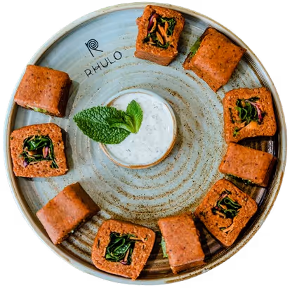 Teller mit neun gebackenen Quadraten mit Gemüsefüllung und einem Becher mit weißem Dip, garniert mit frischer Minze.