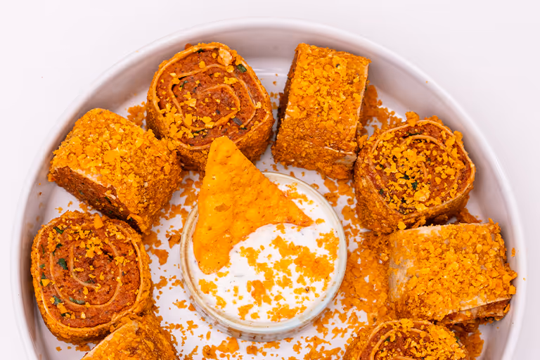 Teller mit würzigen gerollten Snacks, umgeben von einem Dip mit einem Snack darauf und knusprigen Brotkrümeln.