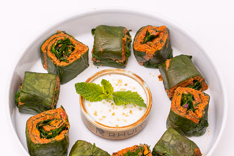 Grüne Blätter gerollt mit einer roten Füllung, arrangiert um eine Schale mit weißem Dip, garniert mit Minzblättern.