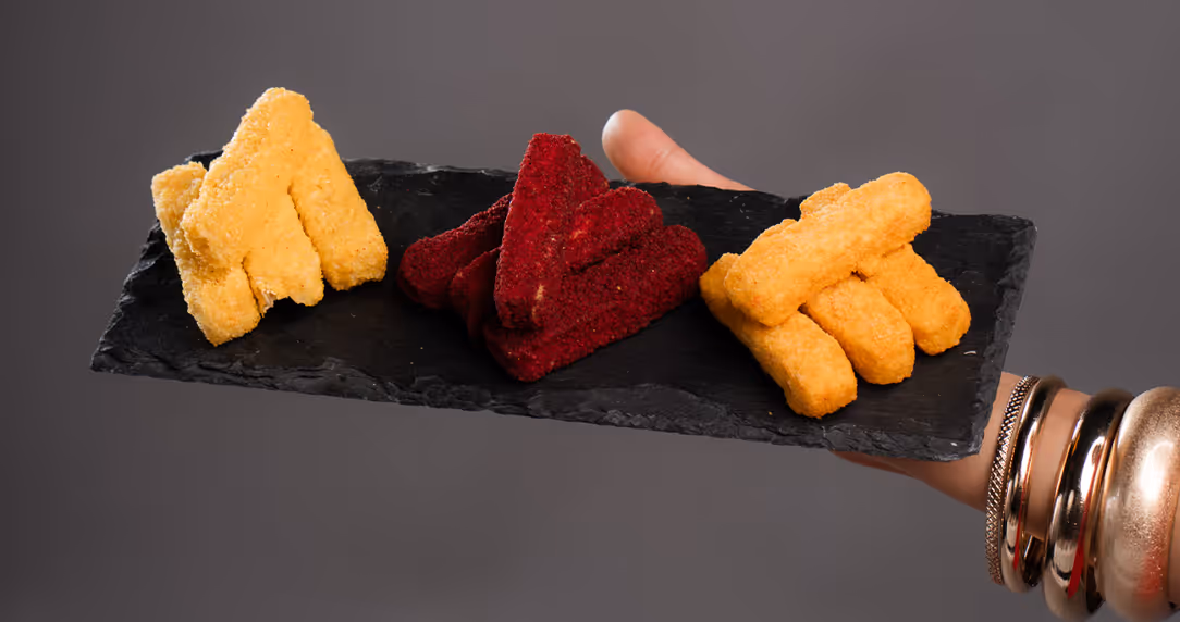 Hand hält eine schwarze Schieferplatte mit drei Buchstaben aus Lebensmitteln in Gelb, Rot und Orange.