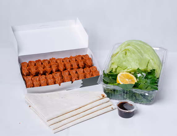 Packung mit rohem türkischem Bulgur-Teigfleisch, Fladenbrot, Salat, Minze, Zitrone und Dipsauce.