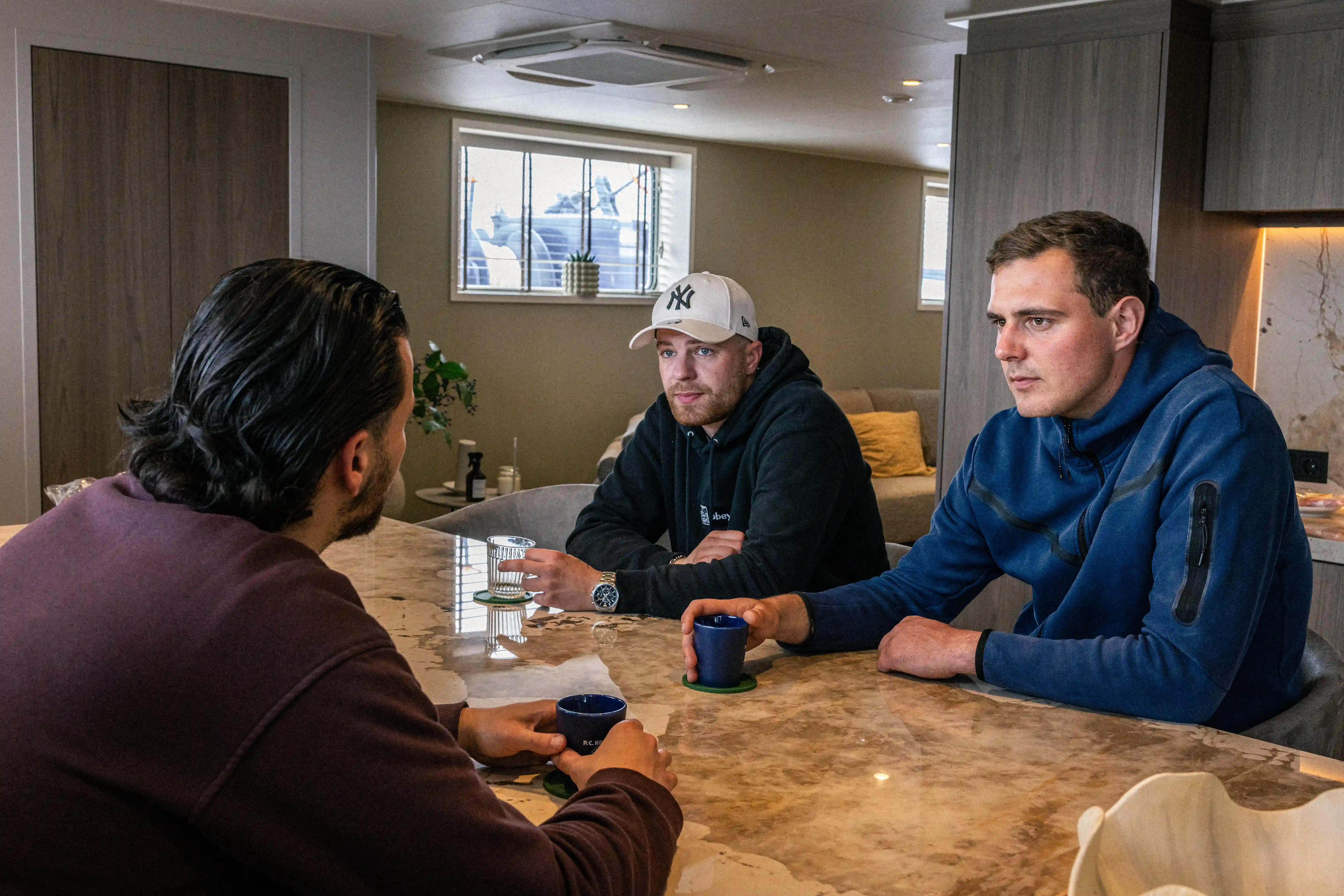 Drie bemanningsleden van Mercurius die koffie drinken in de moderne woonruimte aan boord van een binnenvaartschip
