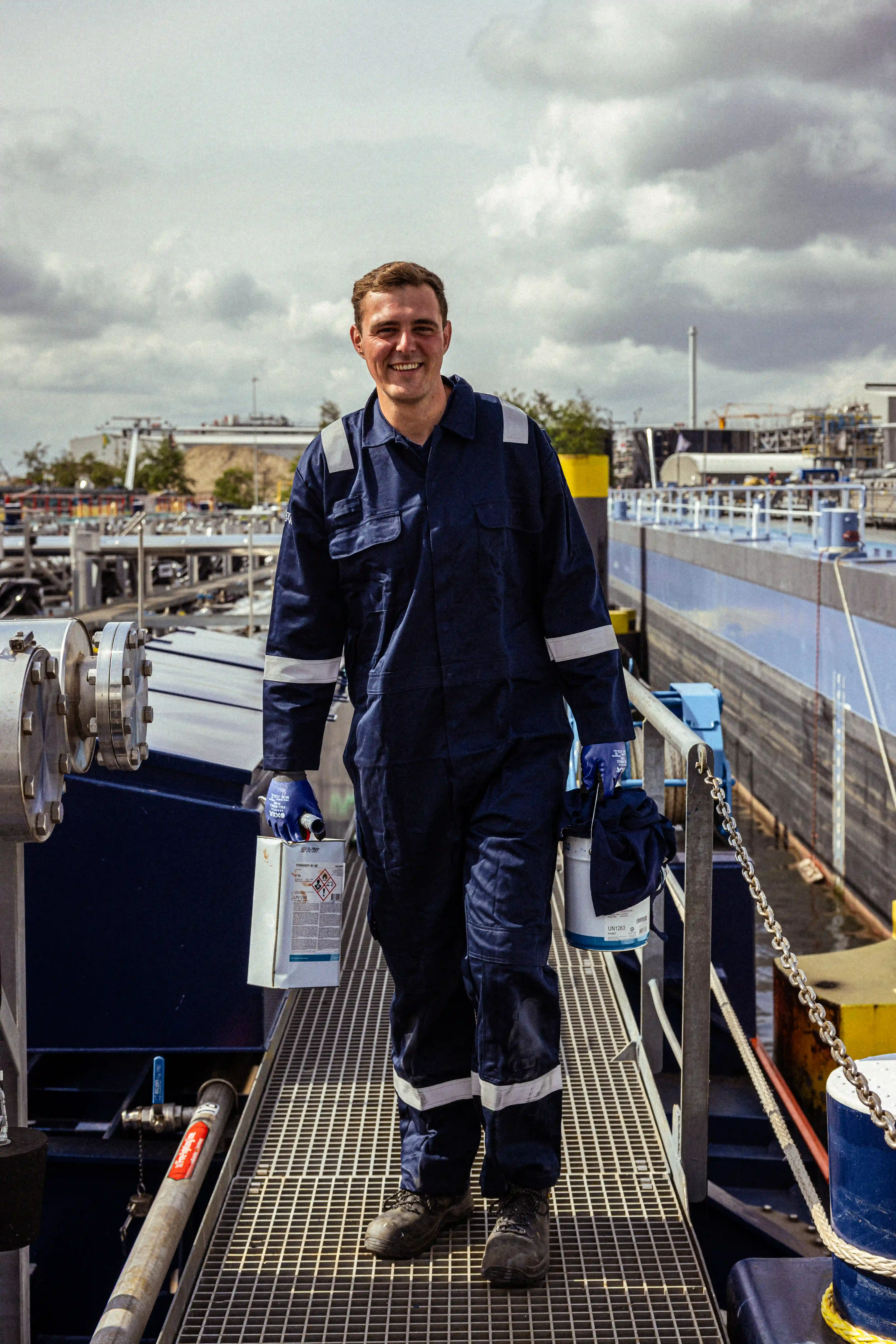 Een medewerker van Mercurius, gekleed in een blauwe overall, op het dek van een binnenschip in een industriële haven.