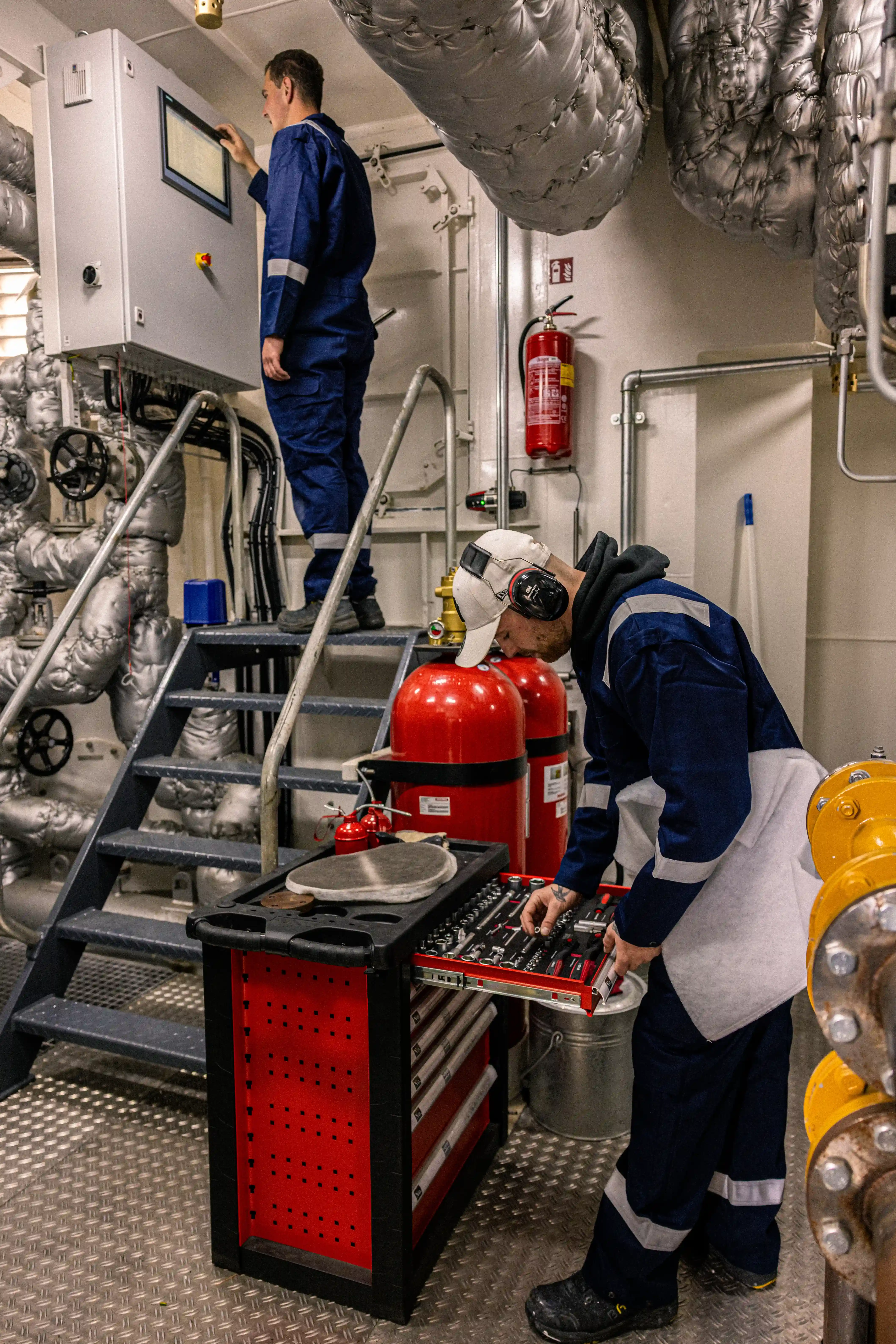 Twee technische medewerkers van Mercurius aan het werk bij een controlepaneel en gereedschapskar in de machinekamer van een binnenschip