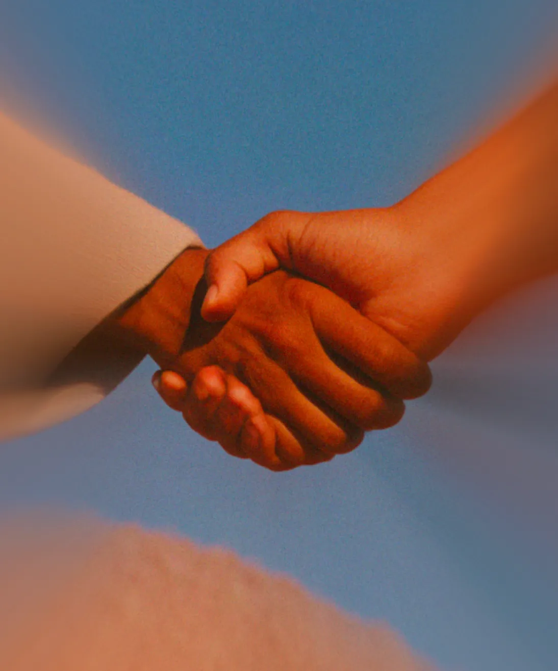 Close-up of two hands clasped together against a blue sky background.