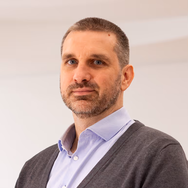 Porträt Foto von einem Mann mit Bart und kurzen Haaren und einem Hemd mit Strickpulli.