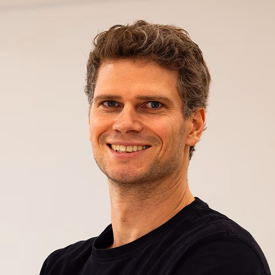 Portraitfoto von einem Mann der lächelt mit kurzen lockigen Haaren und einem schwarzen Pulli.