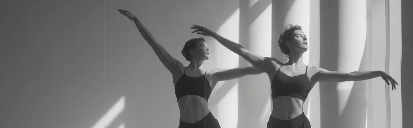 Two women in black sportswear gracefully dancing near a window with sunlight casting shadows.