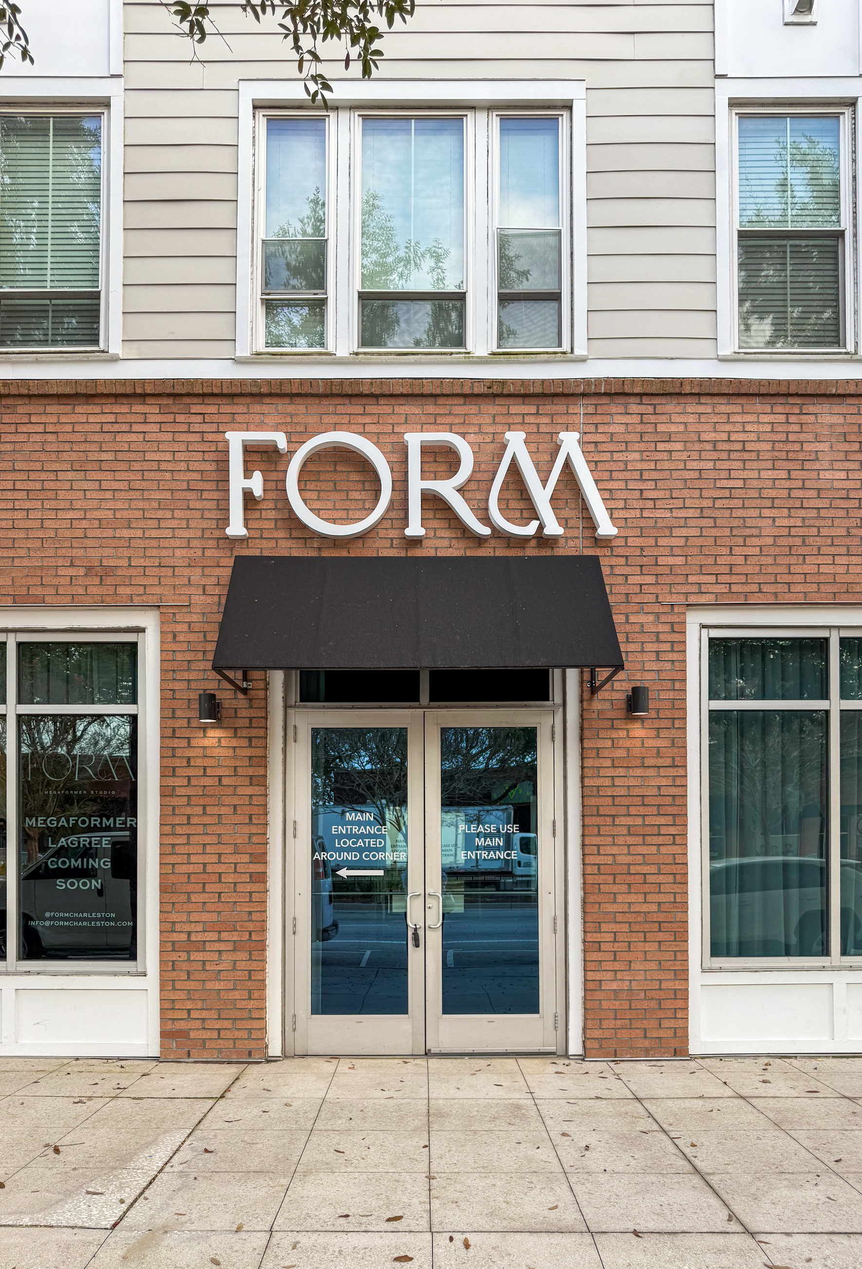 Brick storefront with 'FORM' sign above double glass doors and a black awning, windows on both sides, and text directing main entrance around the corner.