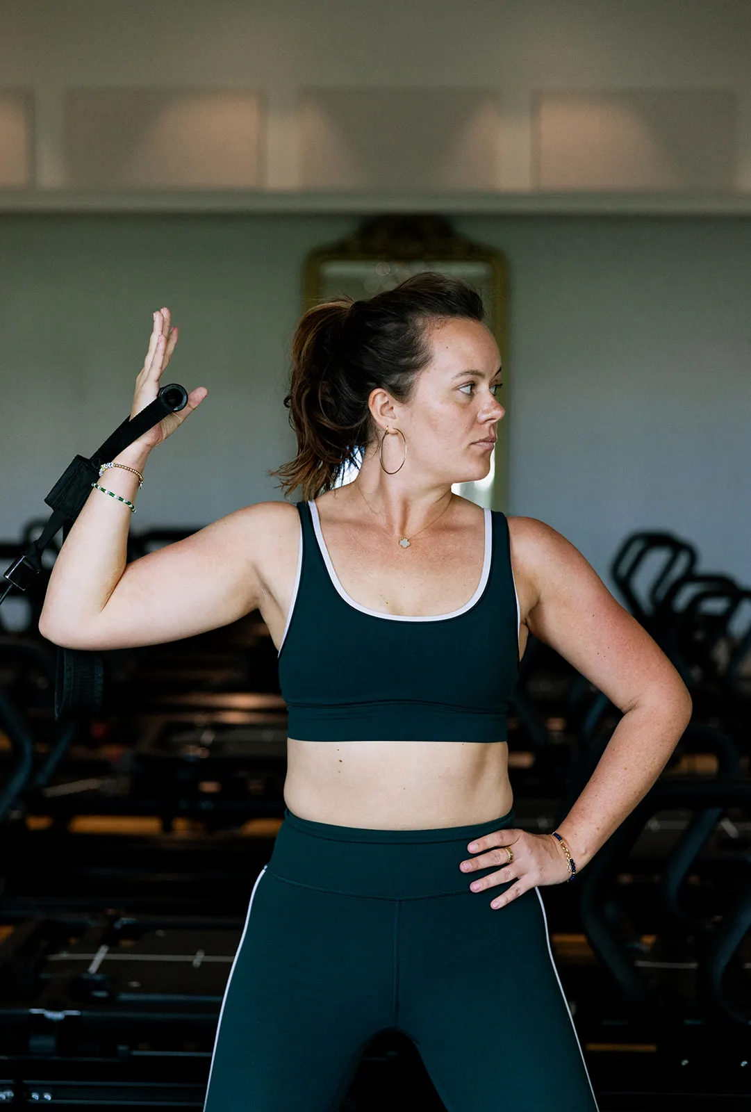 Woman in workout gear using a resistance band for an arm stretch in a gym setting.