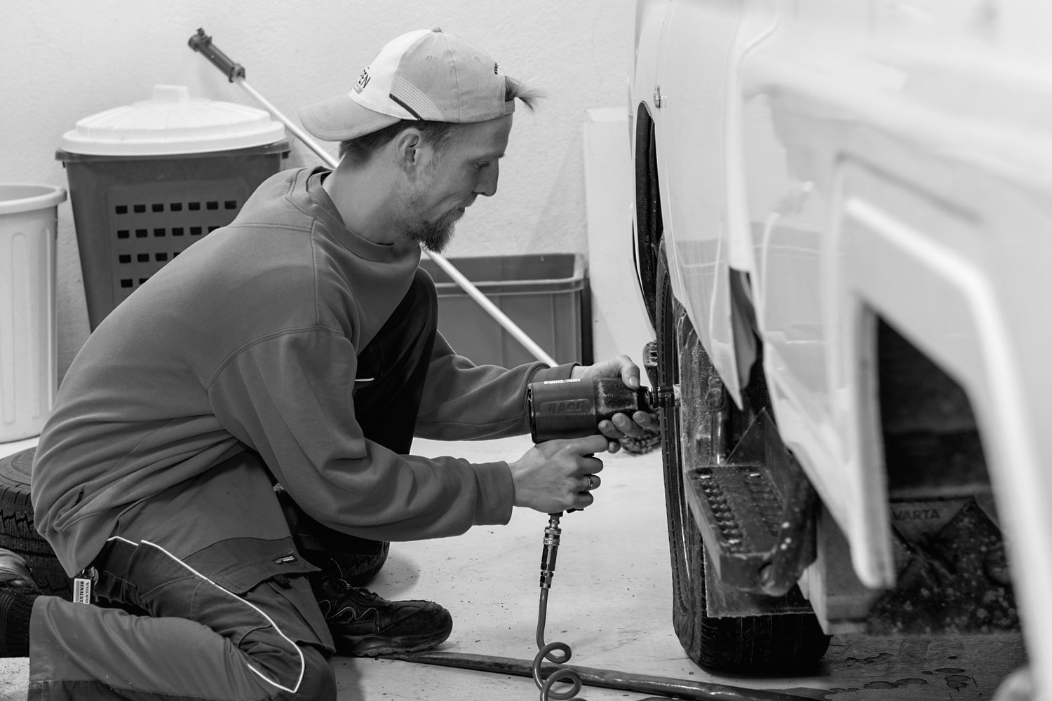 Mekaniker i caps som bruker en luftdrevet muttertrekker på et bilhjul innendørs.