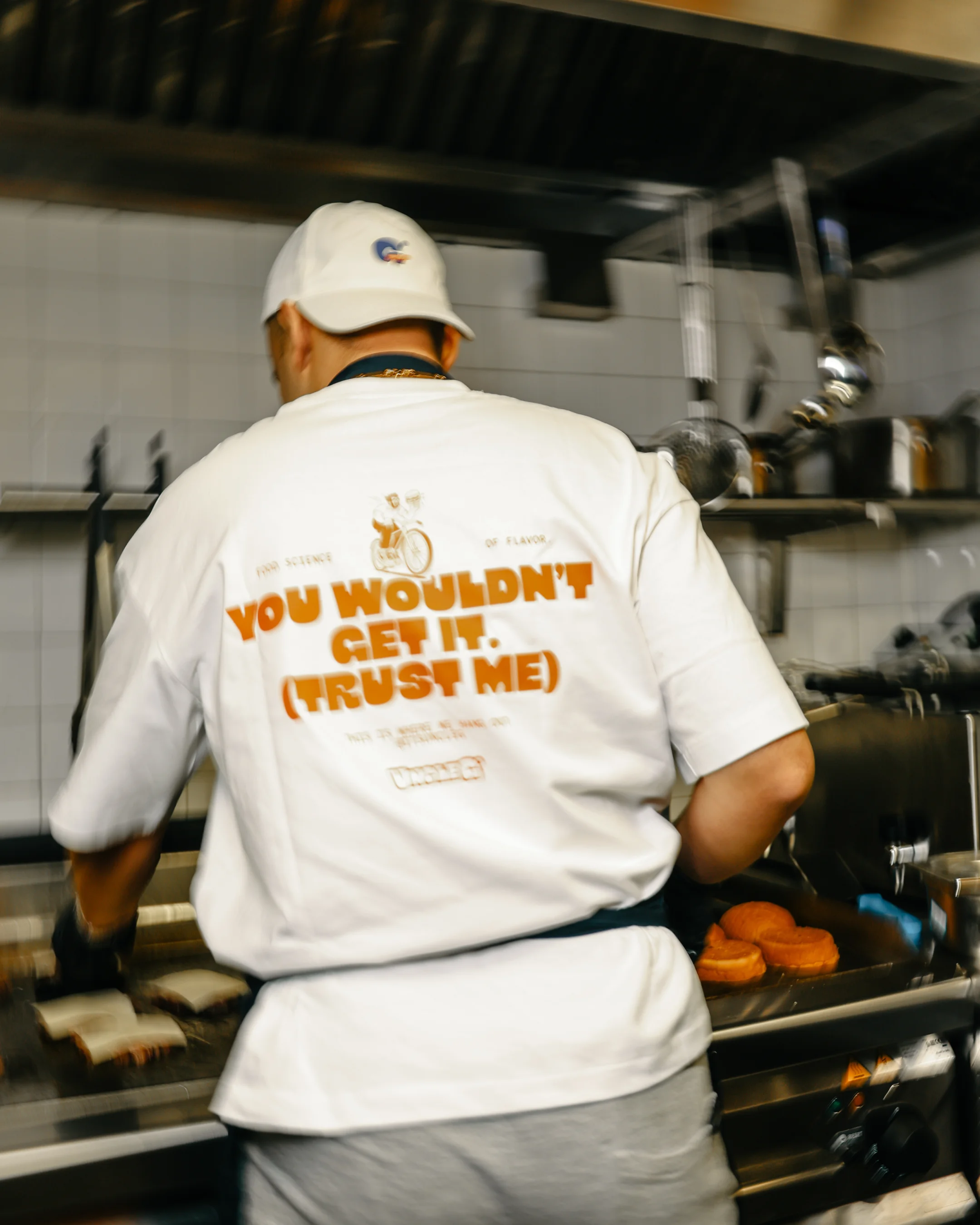 Person wearing a white shirt and cap cooking sandwiches on a grill in a kitchen.