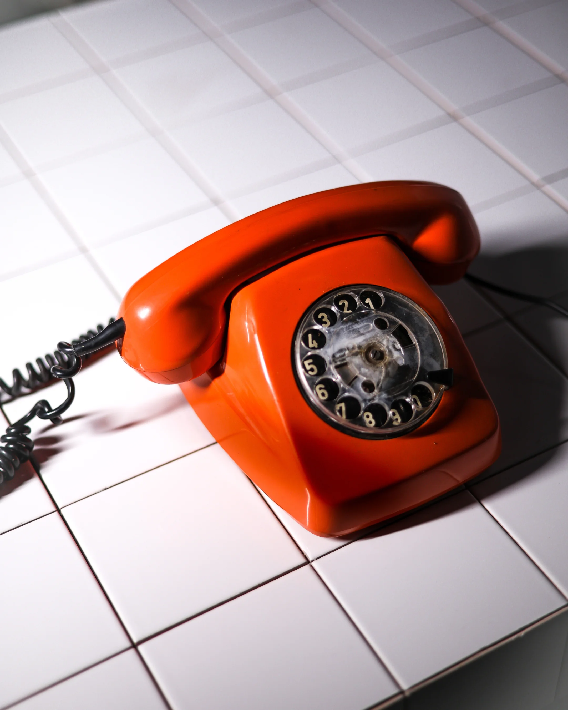 Retro orange rotary dial telephone on white tiled surface.