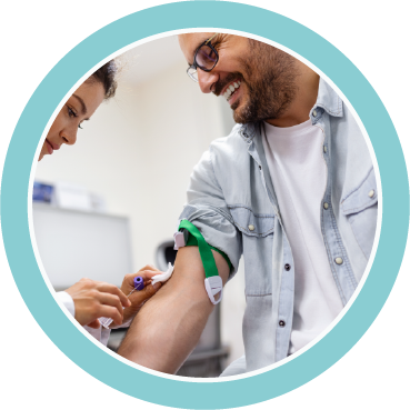 Healthcare professional drawing blood from a smiling man's arm with a green tourniquet in a clinical setting.