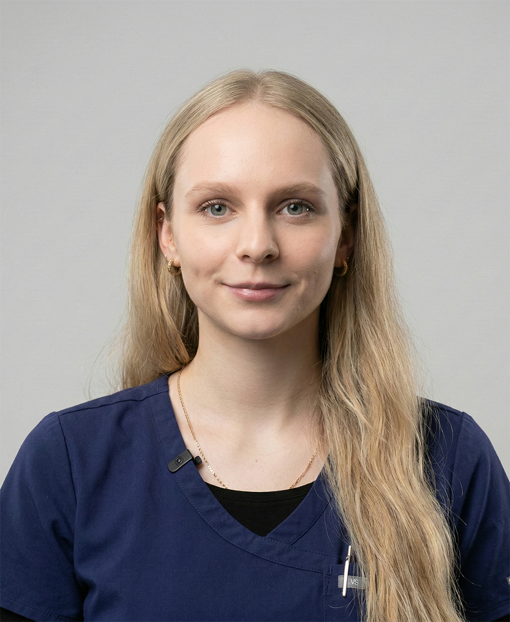 Young woman with long blonde hair wearing a navy blue medical scrub top and a microphone clip.