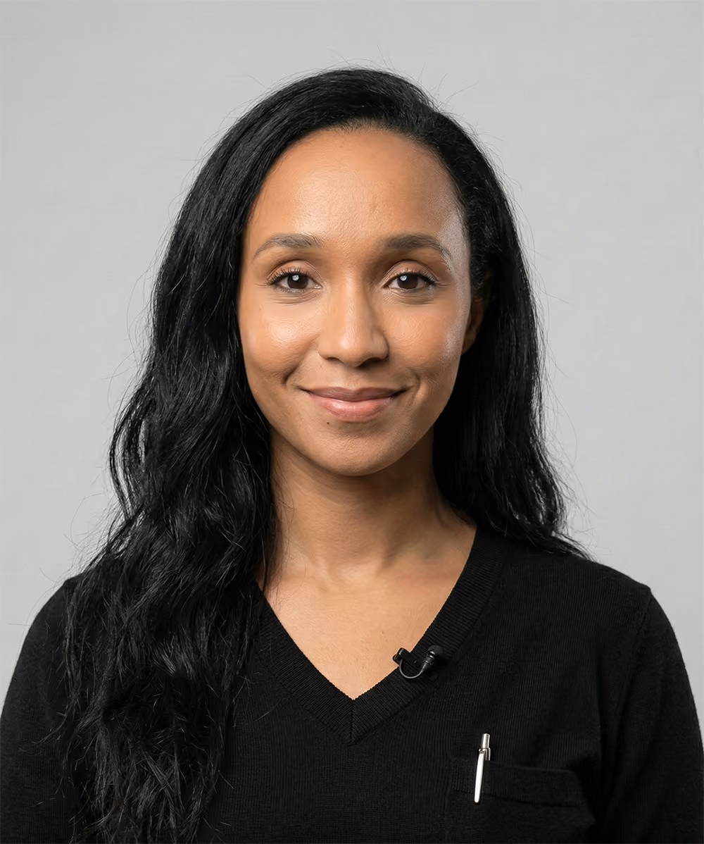 Portrait of a woman with long black hair wearing a black V-neck sweater and a small microphone clipped on it.