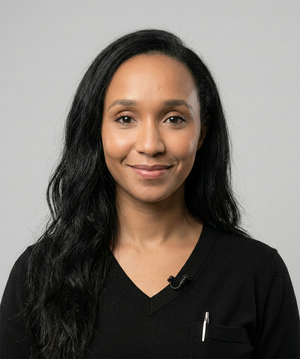 Portrait of a woman with long black hair wearing a black V-neck sweater and a small microphone clipped on it.