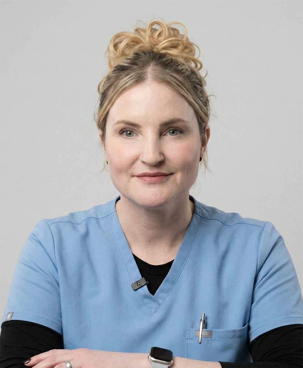Portrait of a woman wearing a light blue medical scrub top, black undershirt, and an Apple Watch, sitting with arms crossed.