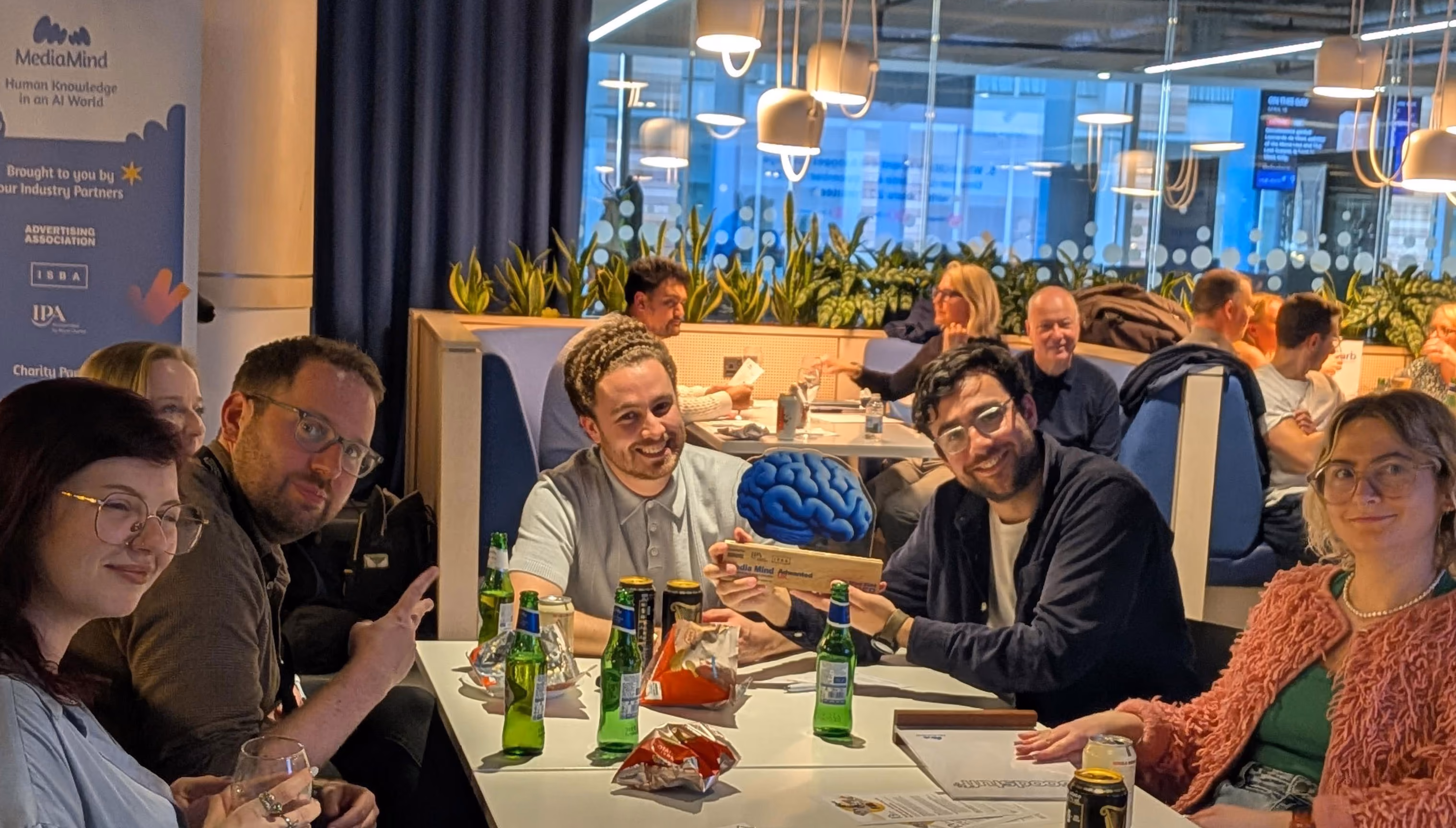 Group at table celebrating with blue brain-shaped award and drinks in a modern lounge area.