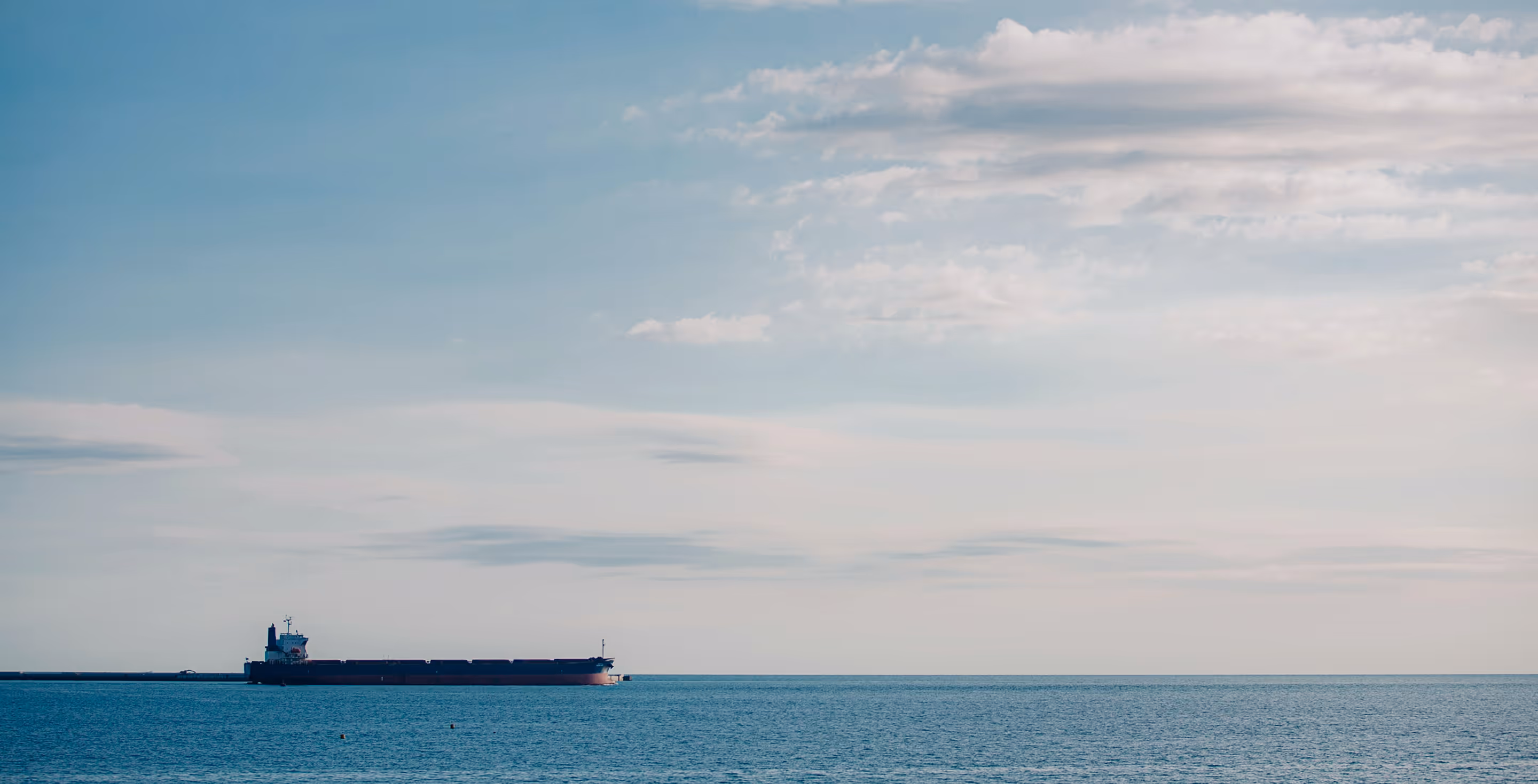 Large cargo ship sailing on a calm sea under a lightly clouded sky.