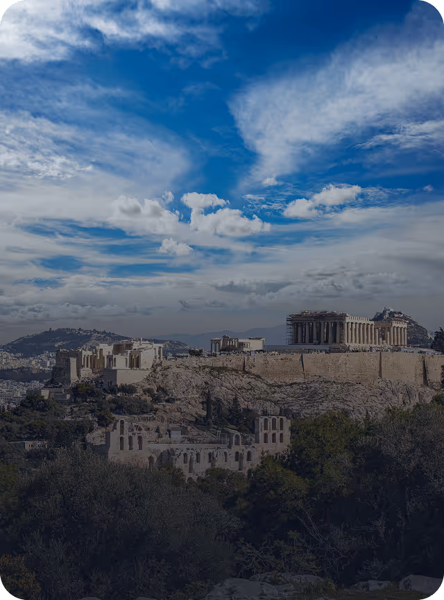 View of the Acropolis in Athens with the Parthenon temple atop a rocky hill under a partly cloudy blue sky.