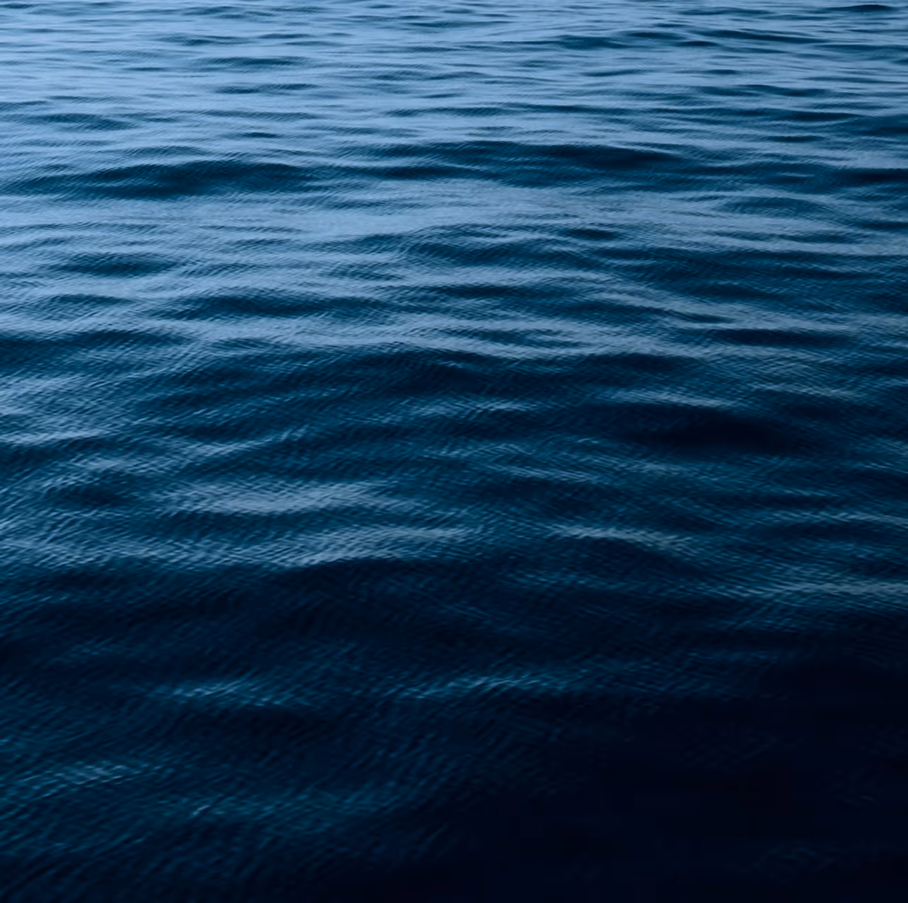 Calm, dark blue ocean water surface with gentle ripples under soft lighting.