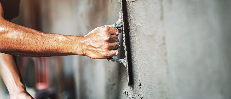 Eine Hand glättet frischen Putz mit einem Glätter auf einer Wand.