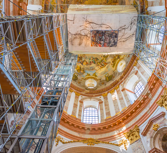 Blick nach oben auf das kuppelgewölbte, barocke Kirchendach mit restaurierenden Gerüsten und Fresken.