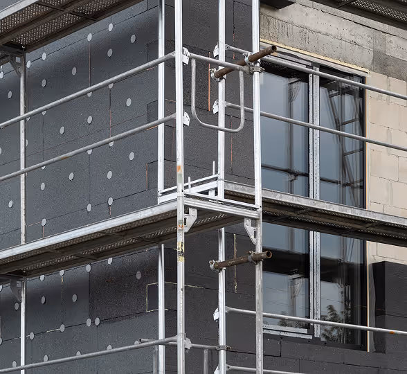 Baustellengerüst vor Wand mit schwarzer Isolierung und Fenster in moderner Bauphase.
