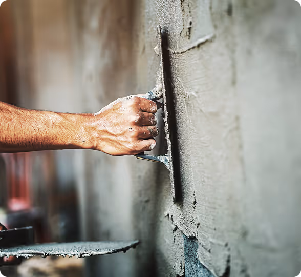 Hand glättet frischen Zement an einer Wand mit einem Kellenwerkzeug.