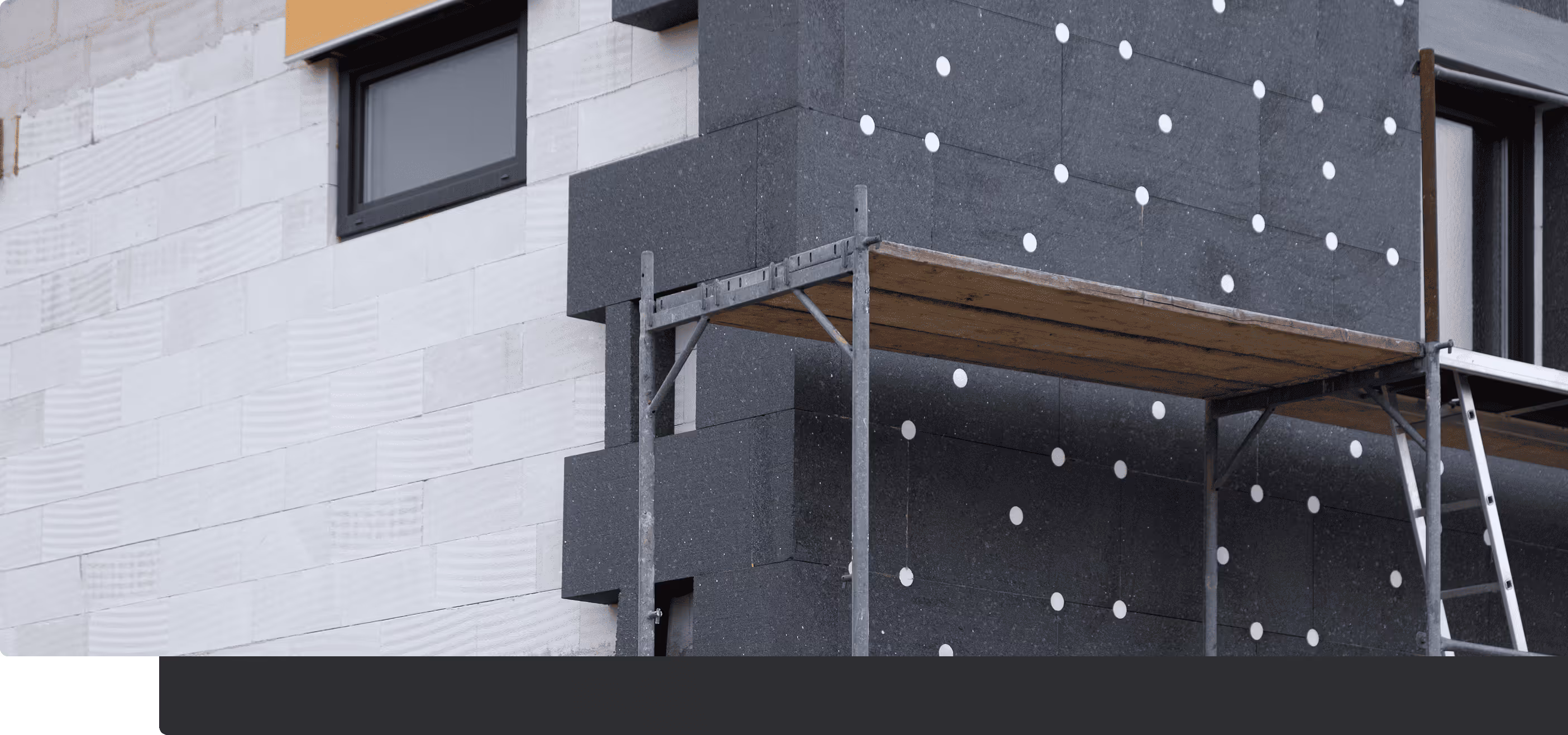 Hausfassade mit grauer und weißer Wärmedämmung und einem Metallgerüst mit Holzplattform.