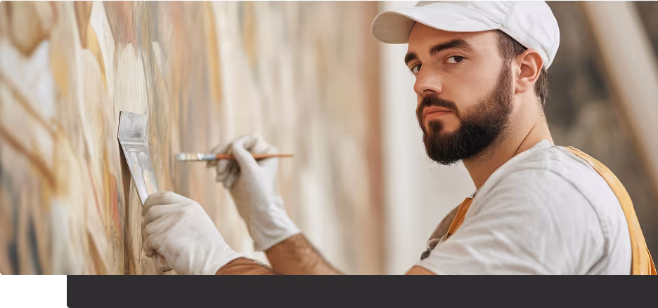 Mann mit Bart und weißer Kappe malt mit Pinsel eine Wandmalerei.