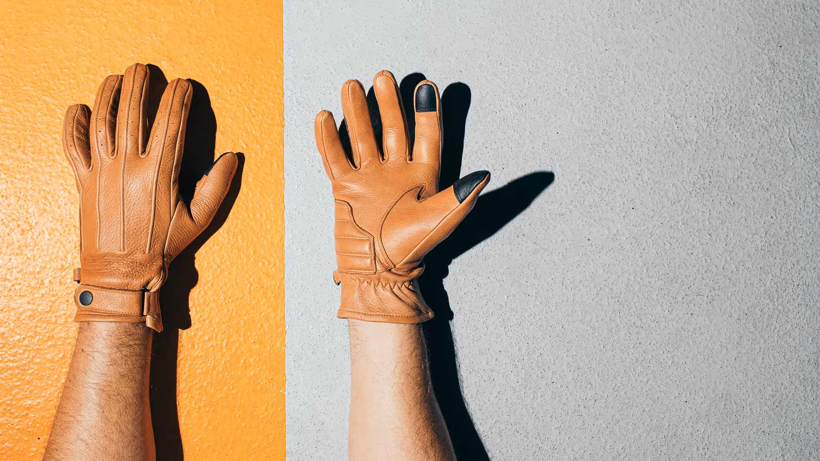 Two hands wearing brown leather gloves placed against an orange and gray textured wall background.