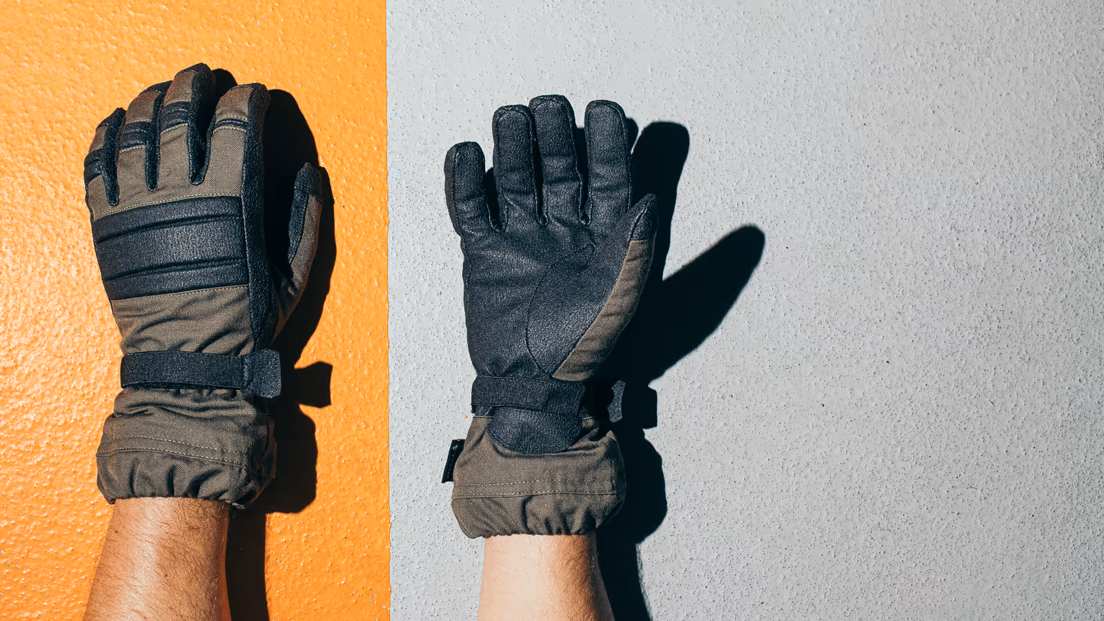 Person wearing padded black and brown gloves, hands pressed against an orange and gray textured wall.