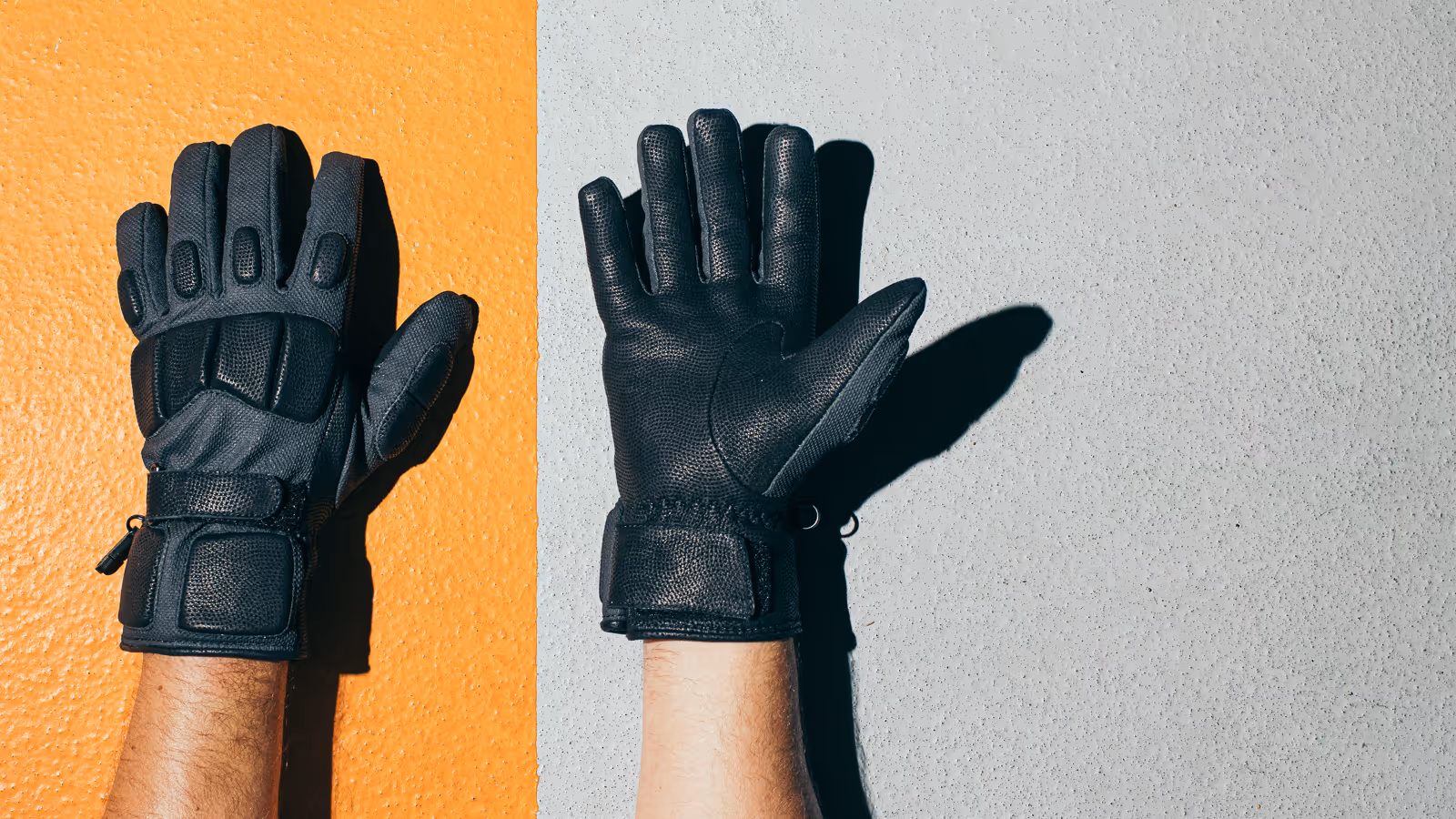 Person wearing black tactical gloves with left hand palm down on orange wall and right hand palm up on gray wall.