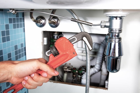 person holding wrench and fixing leaking pipe
