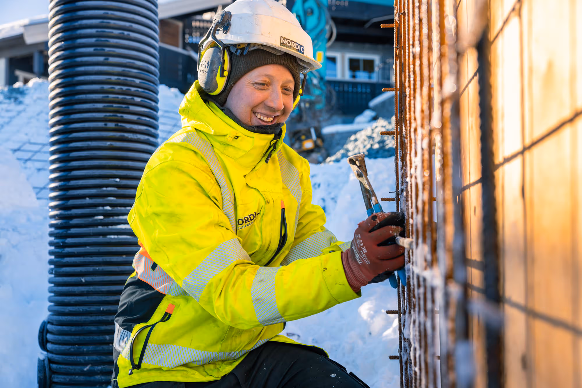 Arbeider i gul refleksjakke og hjelm som jobber med armeringsjern utendørs i snø.
