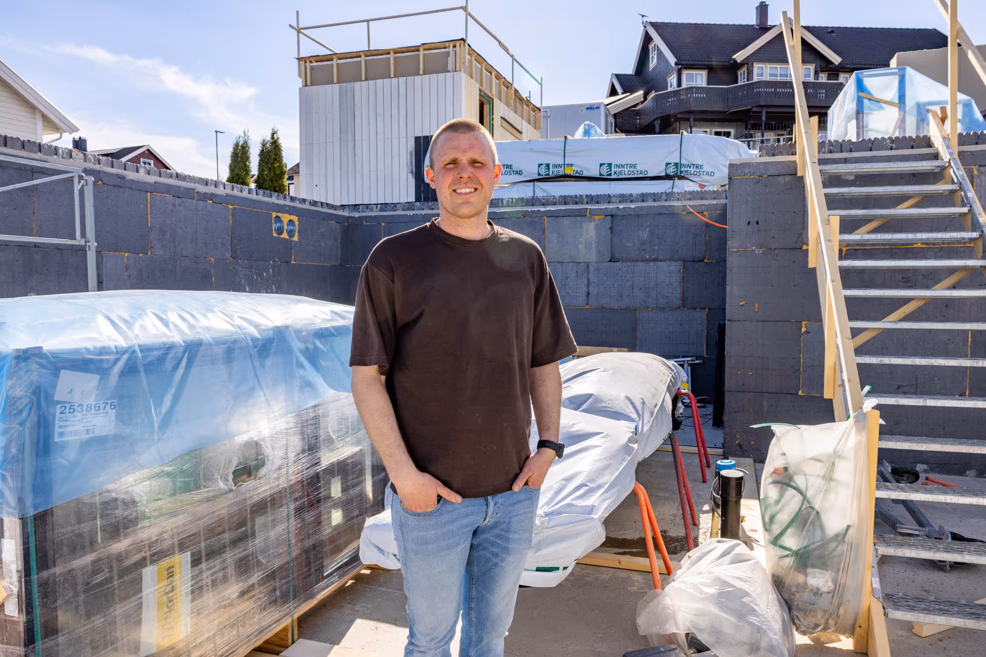 Mann står på byggeplass med sollys, omsluttet av bygningsmaterialer og trapp i bakgrunnen.