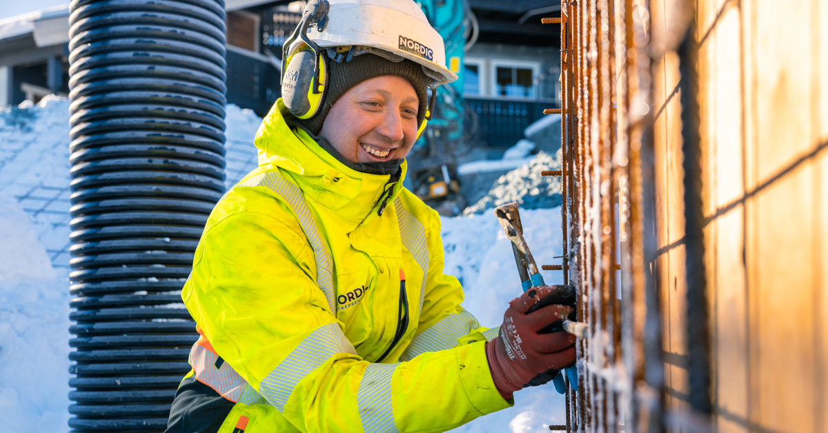 Arbeider i refleksjakke og hjelm som jobber med metall på en byggeplass i vinter.