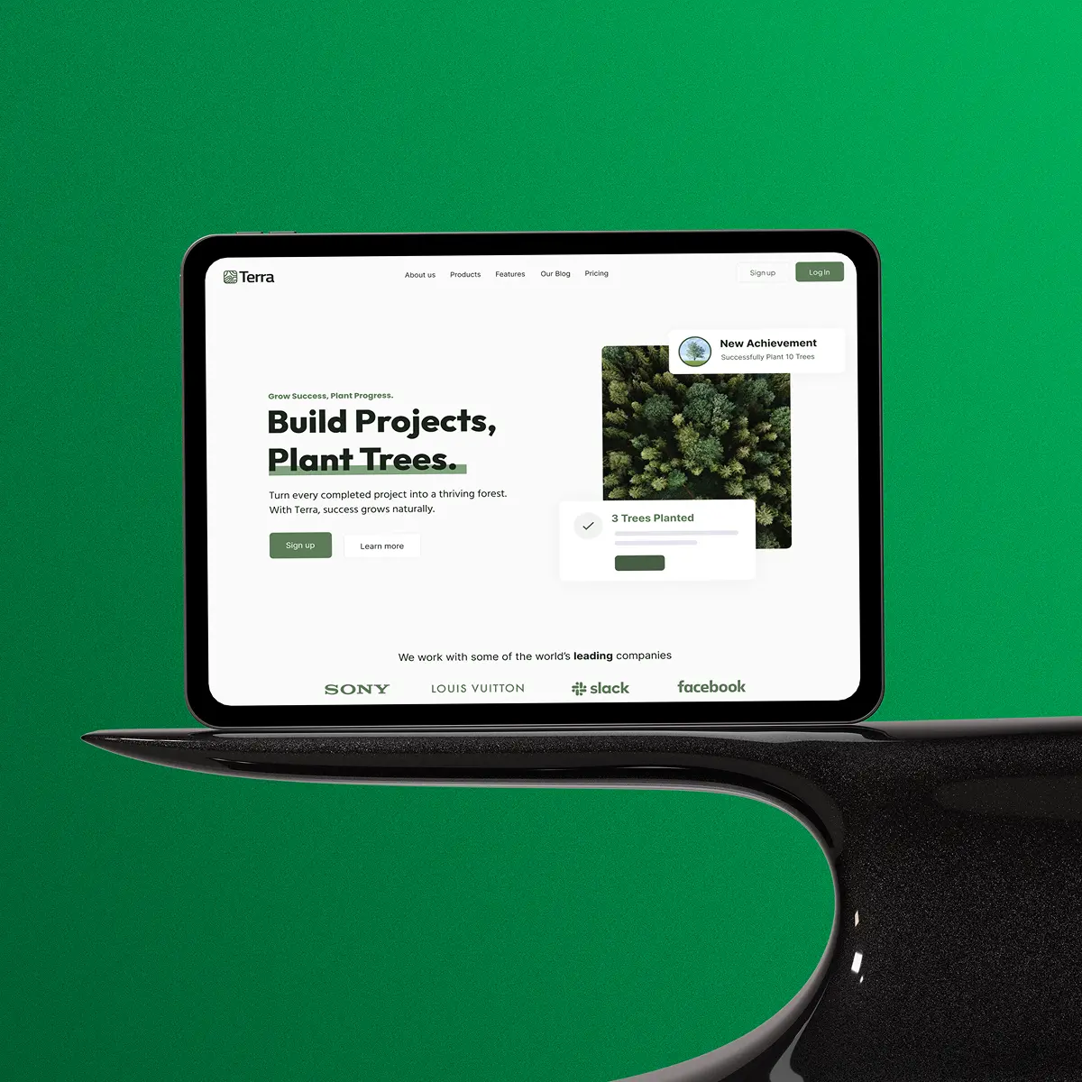 Tablet displaying Terra app website with message about building projects and planting trees, showing forest image and logos of Sony, Louis Vuitton, Slack, and Facebook.