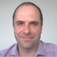 Headshot of a smiling middle-aged man with short hair wearing a light purple shirt.