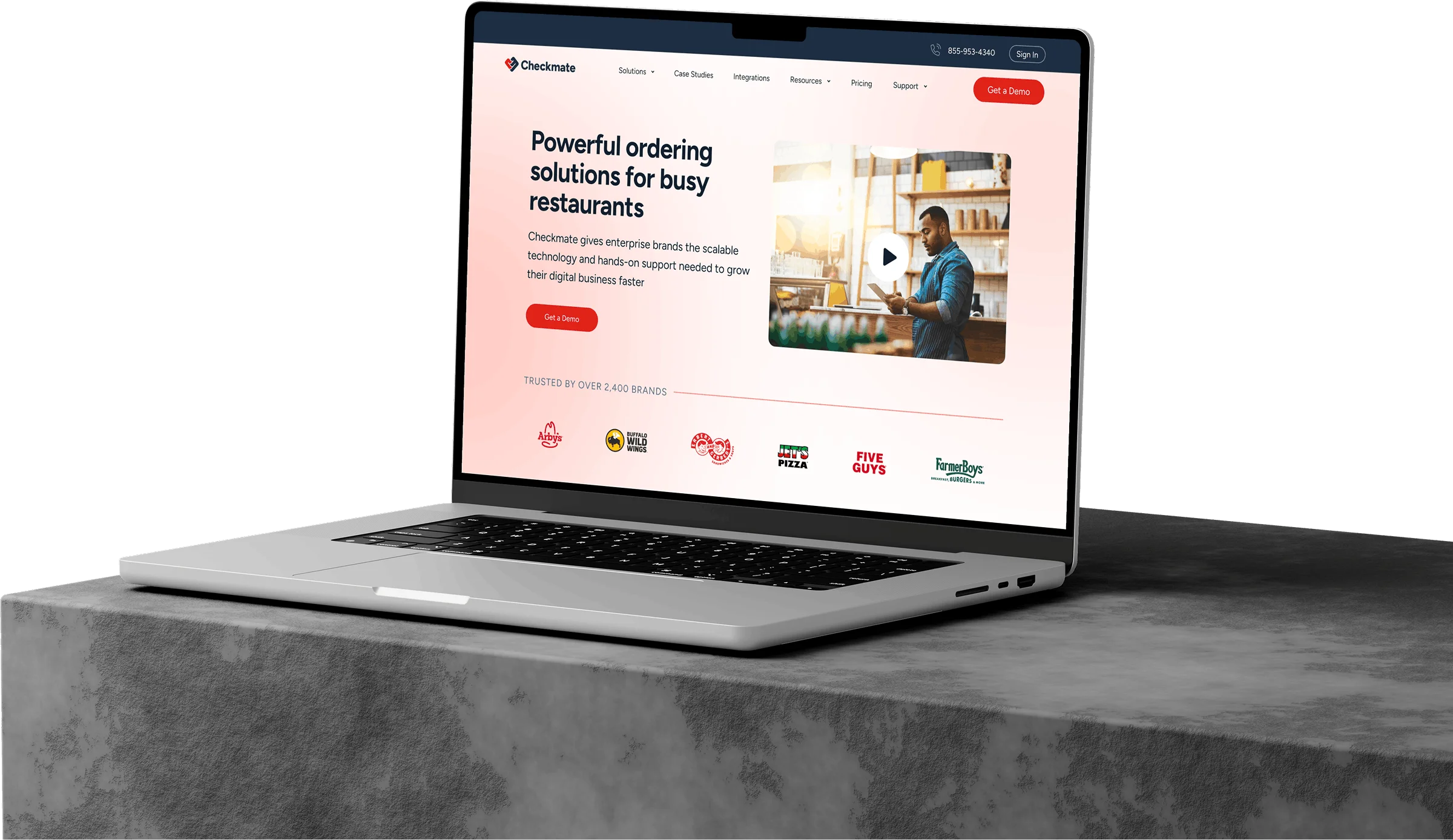 Laptop on concrete surface displaying Checkmate website homepage with ordering solutions for busy restaurants.