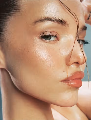 Close-up of a woman’s face with clear skin, natural makeup, and a few strands of hair falling across her forehead.