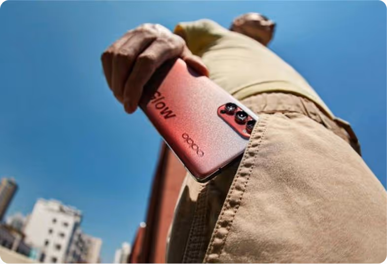 Person holding a red OPPO smartphone with camera visible, standing outdoors against a clear blue sky.