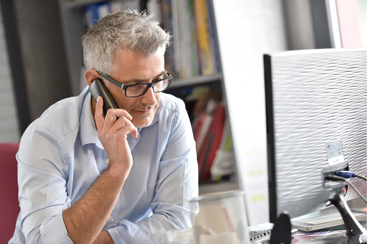 Man with glasses on a mobile phone call at his office desk