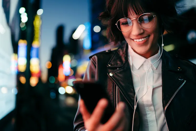 Smiling woman with glasses reading a message on her phone in the city at night