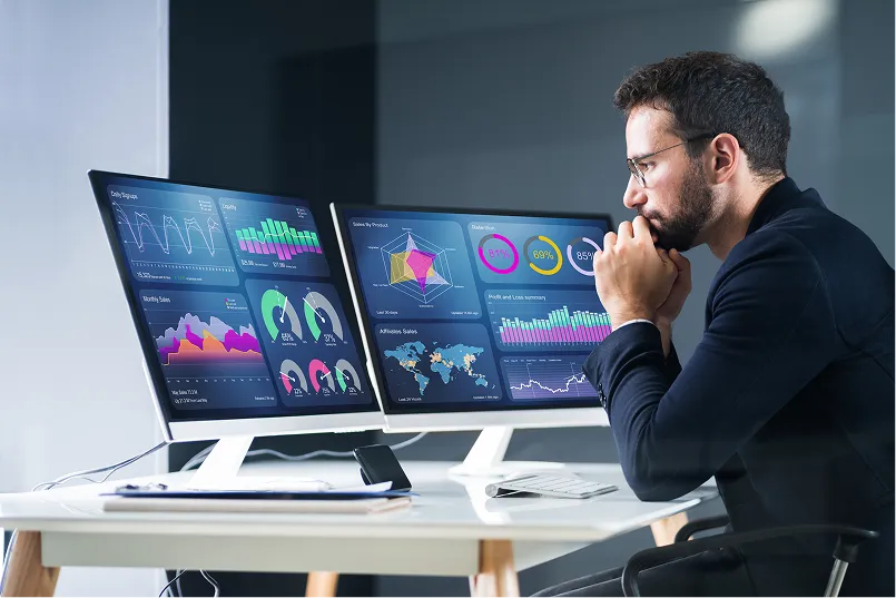 Man analysing data dashboards across two monitors
