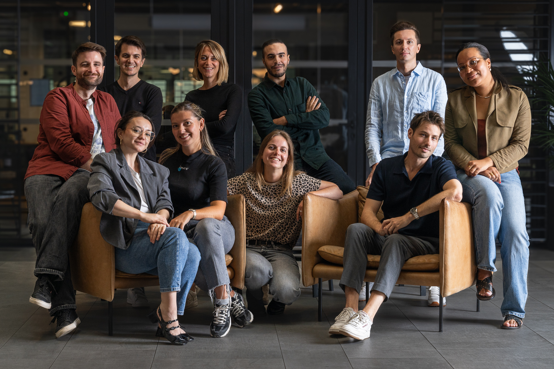 Groupe de dix adultes souriants assis et debout dans un espace de bureau moderne avec deux fauteuils en cuir marron.