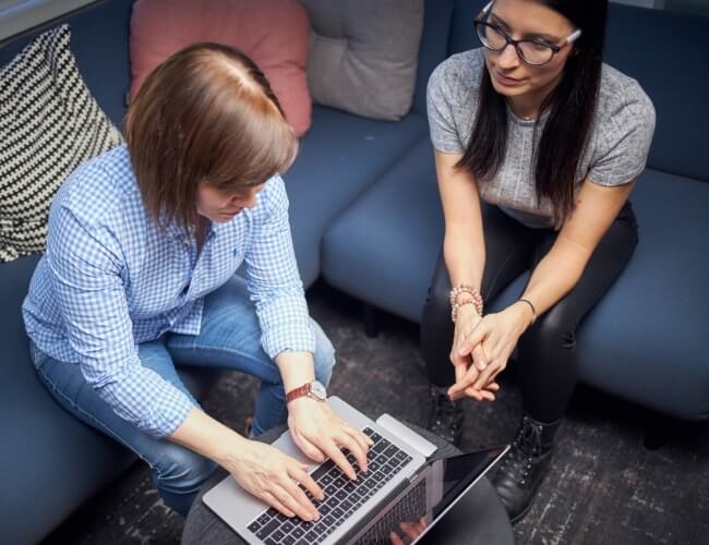 two women sitting, one typing on laptop