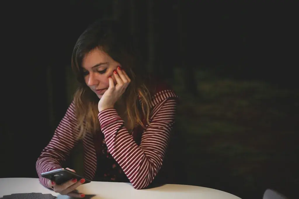a woman sitting in a dark room alone and typing on phone